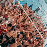 Packed top deck on the Malia Booze Cruise with hands up, drinks flowing and sea views all round—sun-soaked party vibes.