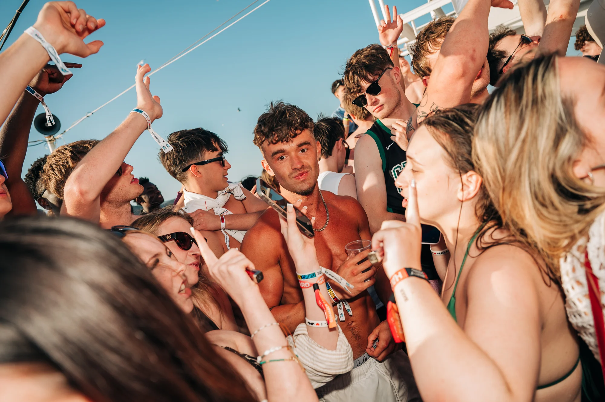 Crowd partying hard under the sun on the Malia Booze Cruise, drinks in hand, music pumping, and energy through the roof.