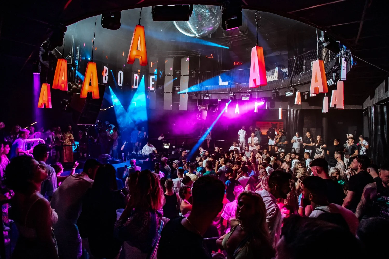 Crowded dance floor at Ibiza Eden club hosting the famous Abode, with vibrant lights and a disco ball, capturing the lively clubbing atmosphere.
