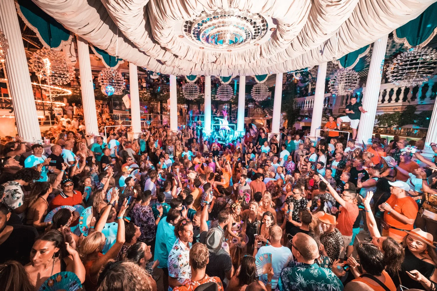 Packed crowd dancing under chandeliers at Es Paradis Ibiza, vibrant lights, summer energy and iconic club vibes.