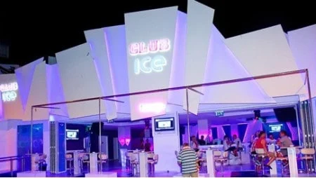 Club Ice in Ayia Napa, with a striking neon facade and lively indoor seating area under purple lighting at night.