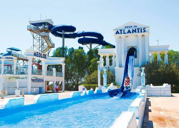 Thrilling water slides at WaterWorld Waterpark in Ayia Napa, Cyprus, with a person sliding down Atlantis ride under clear skies.