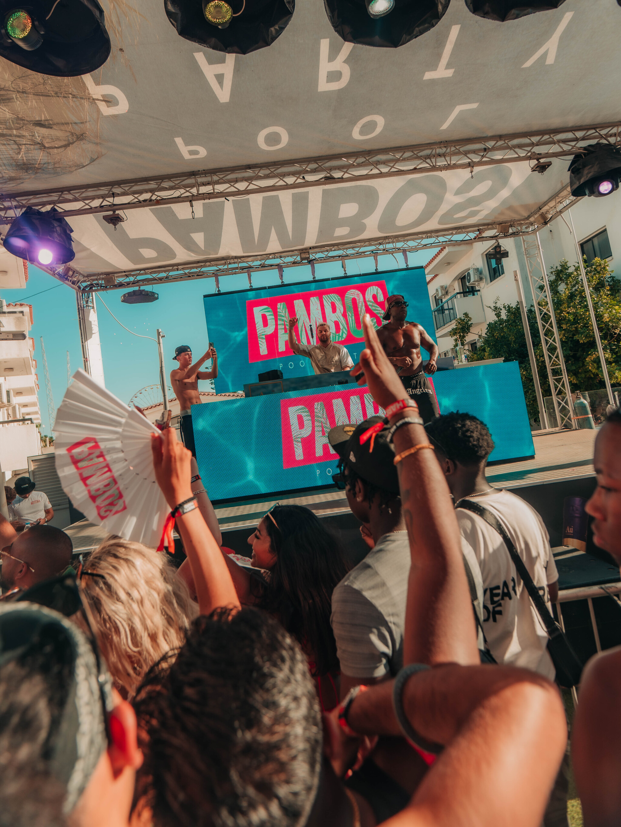 Girls and lads enjoying the Pambos Napa Rocks Pool Party in Ayia Napa, dancing by the stage with DJs performing.