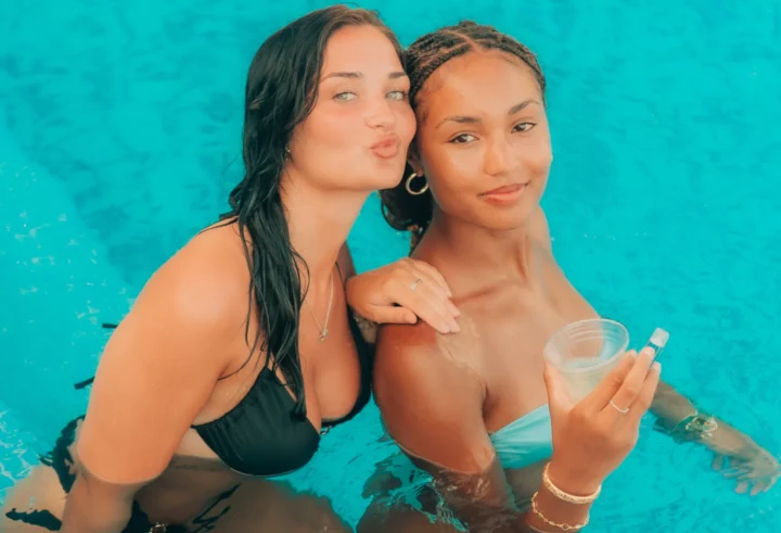 Two girls posing in the pool, one holding a drink, at Sunset Sessions Pool Party in Ayia Napa.