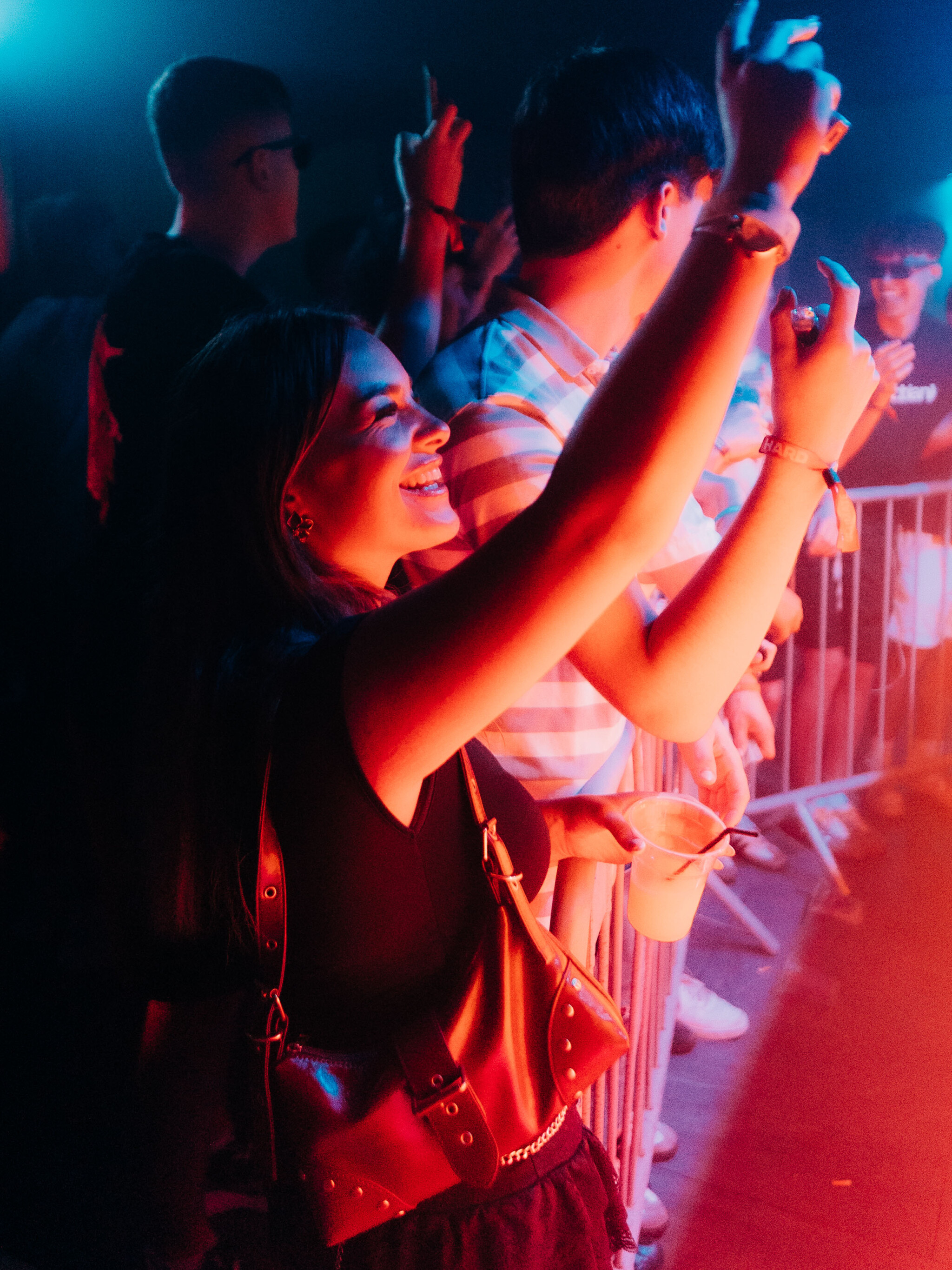 Woman smiling and raising her hand while holding a drink at the House of Tech event in Ayia Napa, enjoying the music and atmosphere.