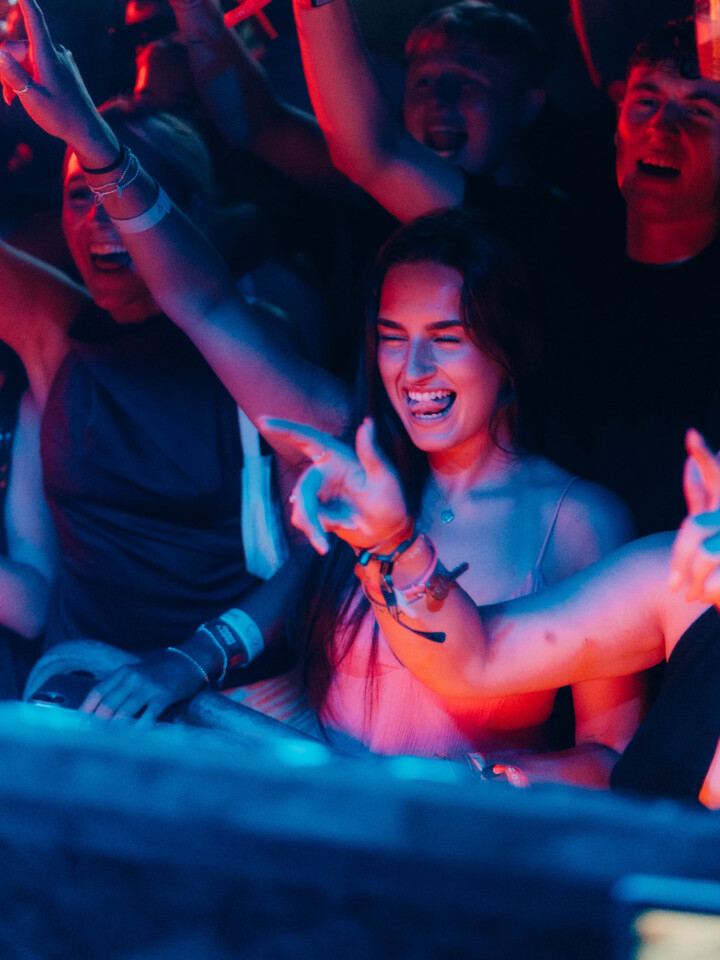 Smiling woman dances in the crowd at the House of Tech event in Ayia Napa, surrounded by friends under vibrant lights.