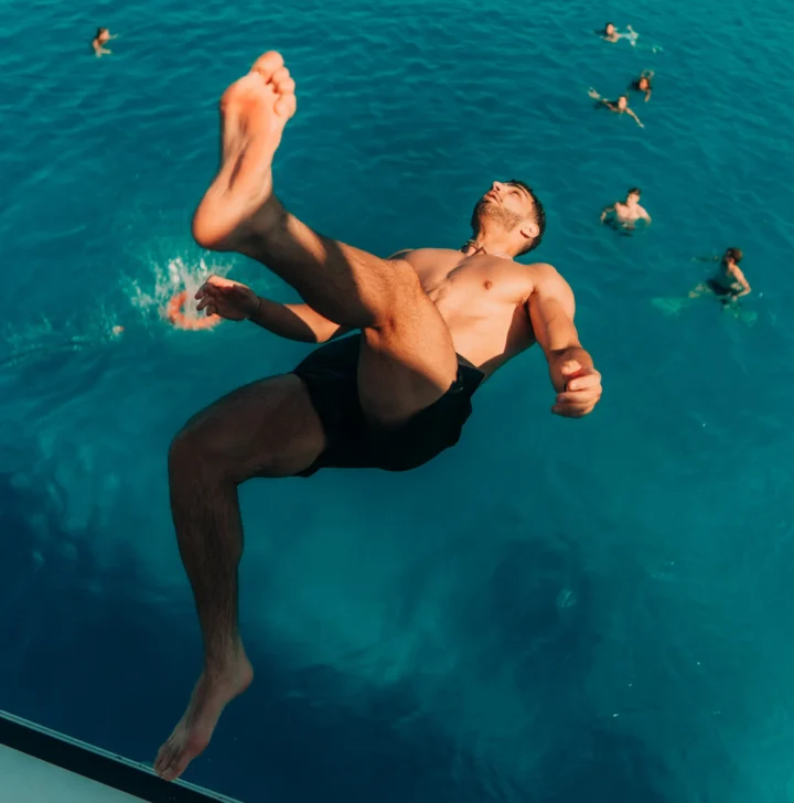 Man mid-air jumping off a boat into the sea at an Ayia Napa boat party with friends swimming in the background