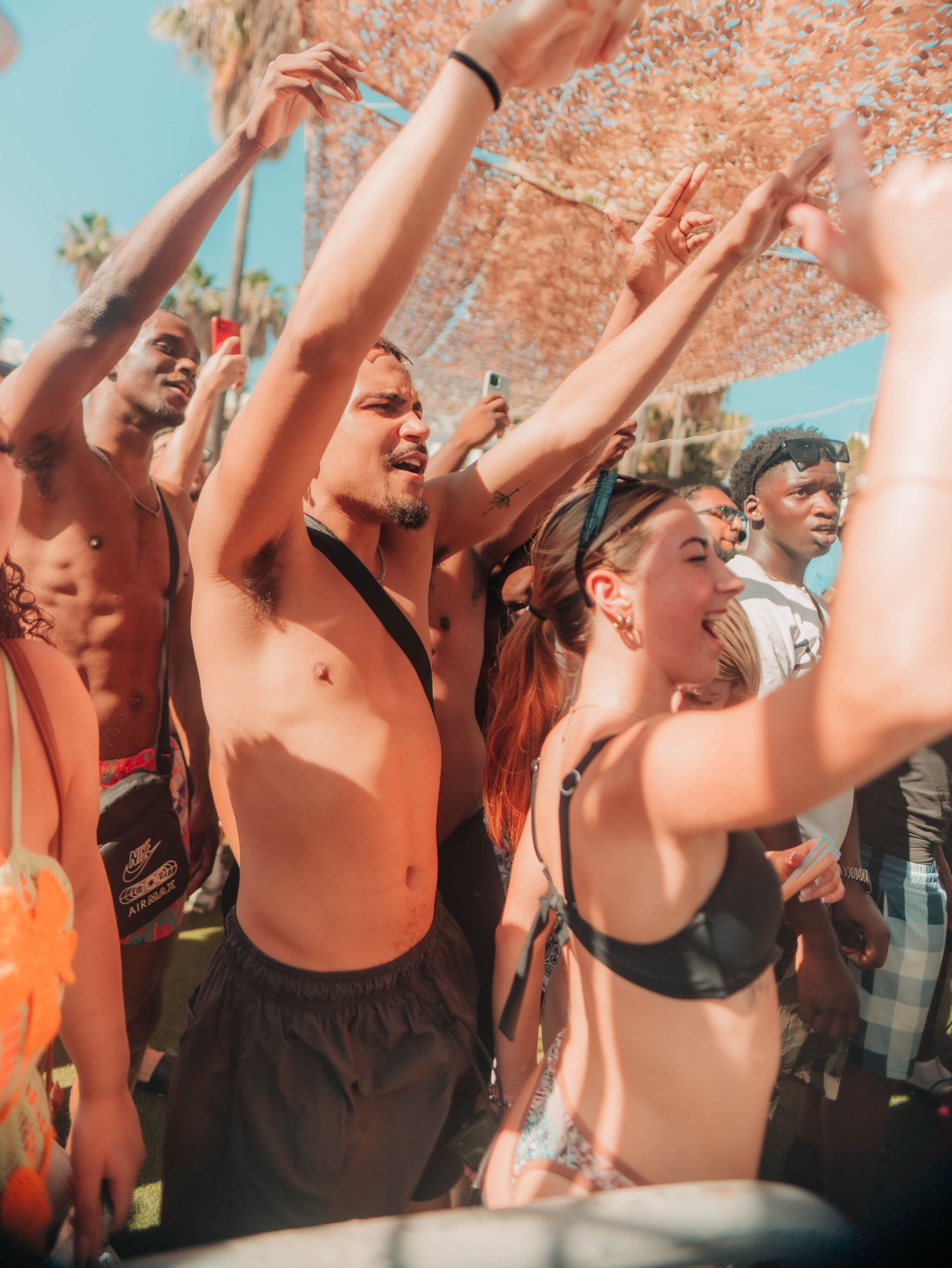 Girls and lads cheering with hands raised in the crowd at Pambos Napa Rocks Pool Party in Ayia Napa under the summer sun.