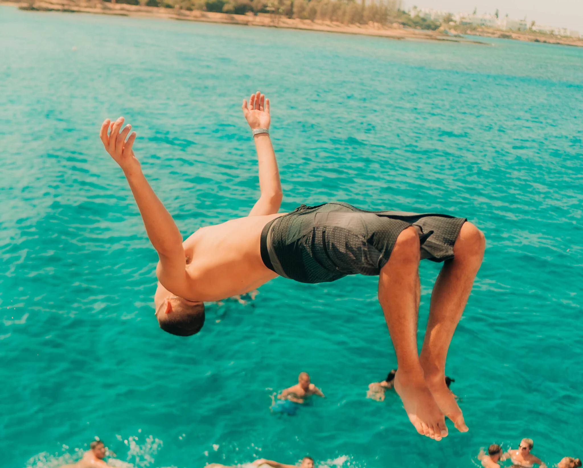 Partygoer backflipping into the sea during an Ayia Napa boat party with friends swimming below