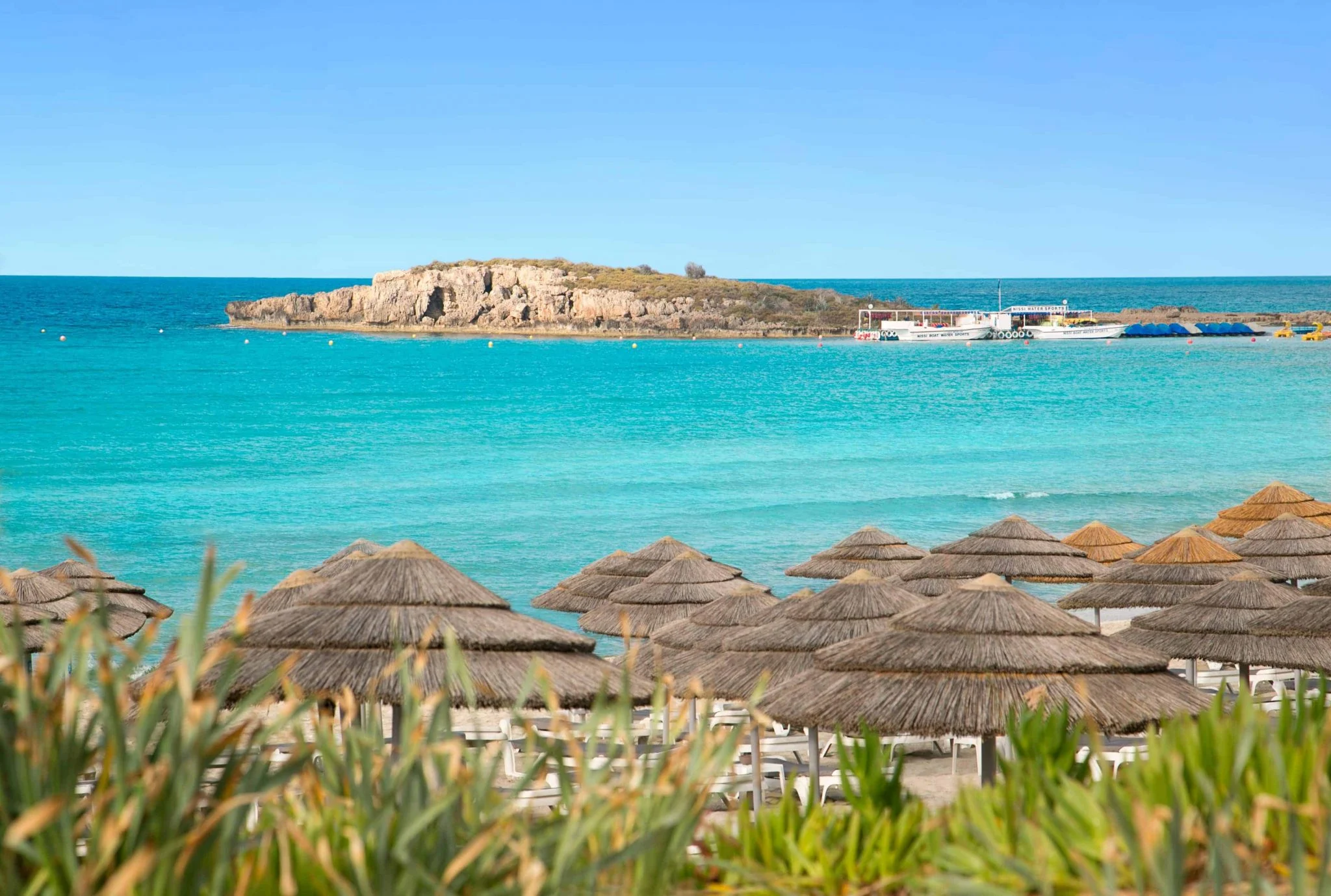 Scenic Nissi Beach in Ayia Napa, with thatched umbrellas and a view over Nissi Bay Island under a clear blue sky.