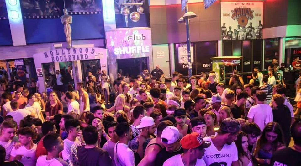 Bustling Club Shuffle in Ayia Napa, with a lively crowd under neon lights and a Hollywood Boulevard entrance at night.