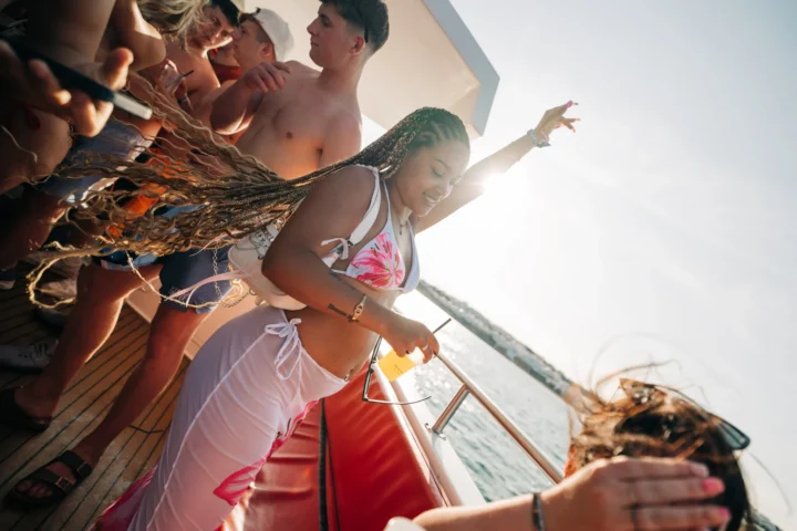 Girl in a white bikini with pink floral design dancing with a drink in hand on deck at the Albufeira Boat Party, enjoying the Algarve sunshine and ocean views.