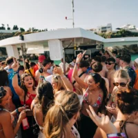 Girls and lads partying on deck at the Albufeira Boat Party in Albufeira, dancing and enjoying drinks under the sun with stunning coastline views.