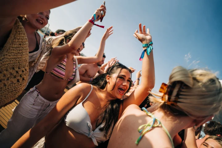 Girls dancing, singing, and raising their hands in the air at the Albufeira Boat Party, celebrating under the summer sun.