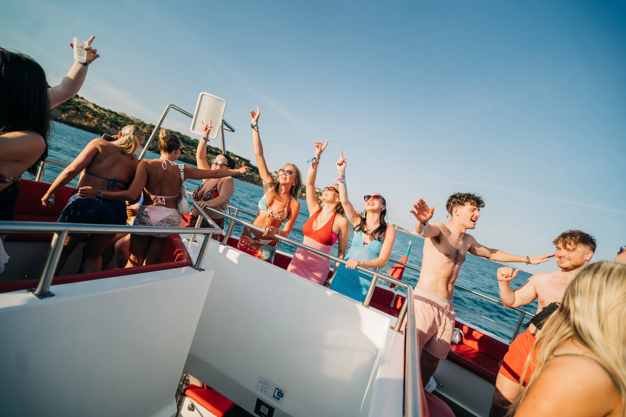 Lads and girls laughing and pointing to the sky on the deck at the Albufeira Boat Party, celebrating under the Algarve sun with ocean views.