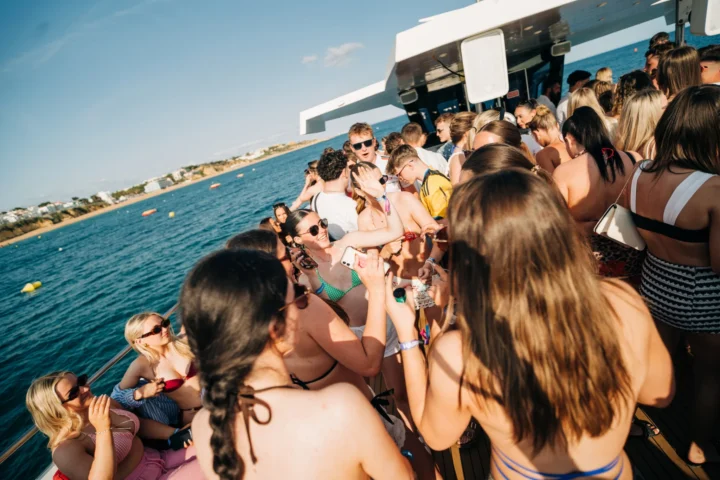 Girls and lads enjoying the Albufeira Boat Party in Albufeira, dancing on deck with drinks, music and stunning ocean views in the background.