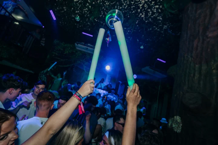 Partygoers waving glow sticks at Club Tropicana Albufeira as the DJ drops beats under jungle lights and disco vibes.