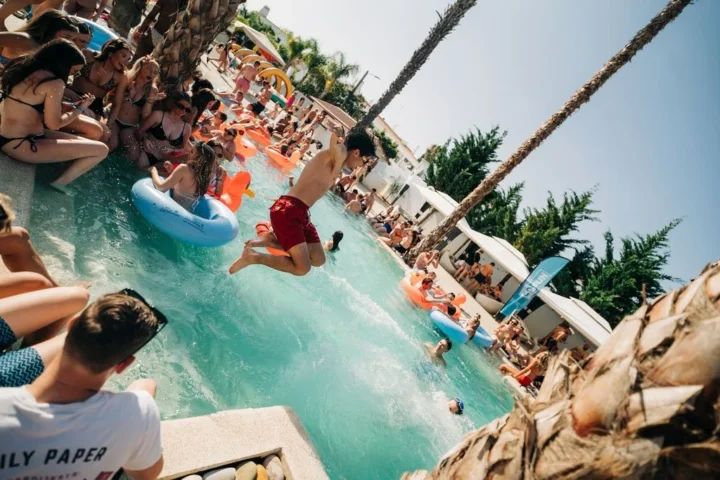 Crowds enjoying the Heaven Pool Party in Albufeira, with people relaxing on inflatables, dancing by the pool, and someone mid-jump into the water.