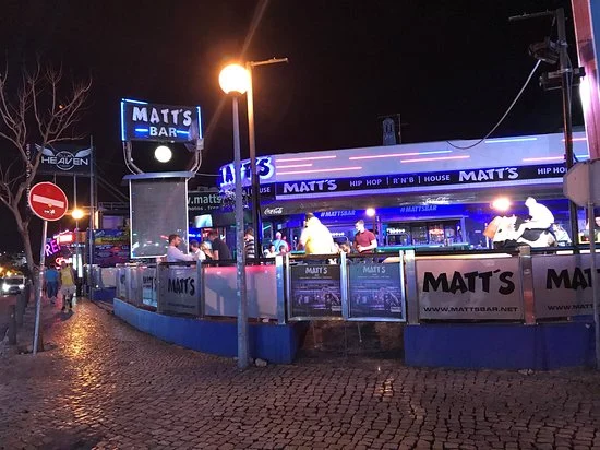 Matt’s Bar, a lively hotspot on Albufeira’s main Strip, with neon signage and a bustling outdoor scene at night.