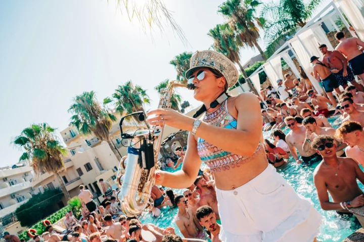 Pool party vibes in Malia as the sax player brings the beats to a crowd of partygoers dancing under the summer sun.