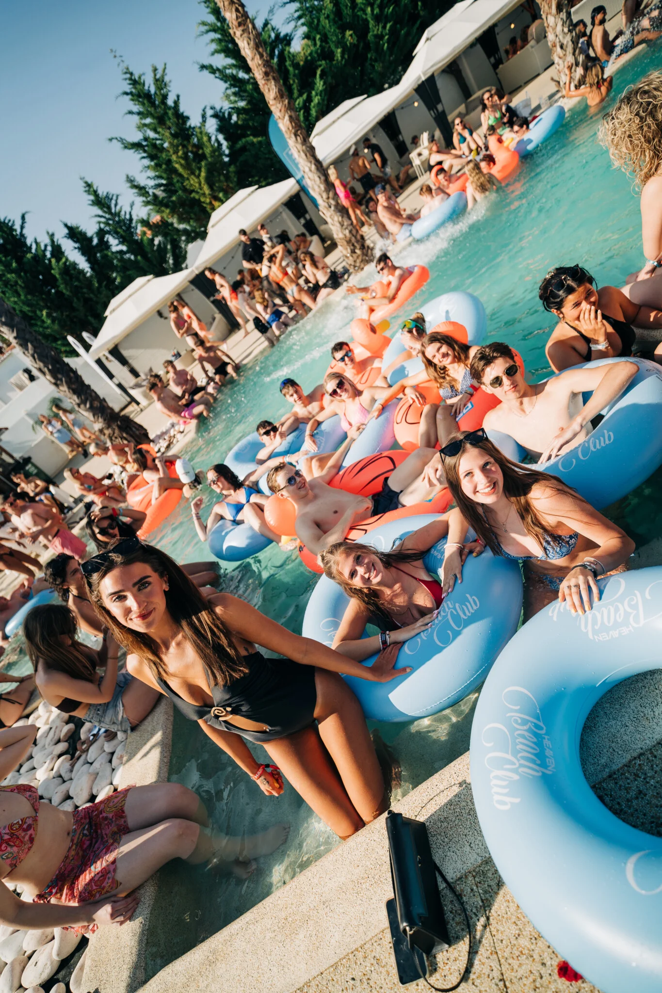 Girls and lads enjoying the Heaven Pool Party in Albufeira, with groups relaxing on inflatables, chatting by the pool.