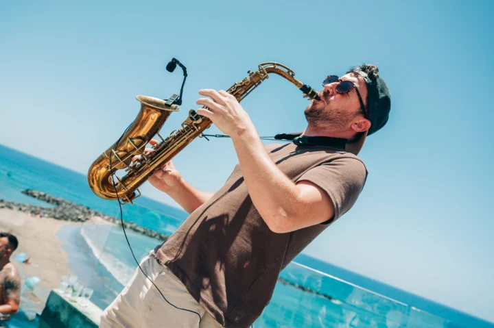 Sax player performing poolside at a Tenerife day party, shades on, ocean views and the crowd soaking up the vibes