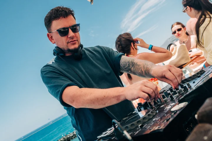 DJ mixing live at a Tenerife boat party, decks in action, ocean backdrop and the crowd locked into the sound