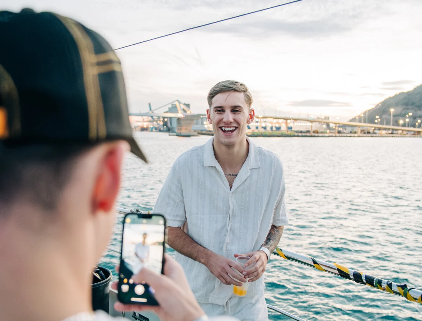 Friends capturing a sunset boat moment in Barcelona as a guy laughs with a drink, setting the vibe for a lively night.