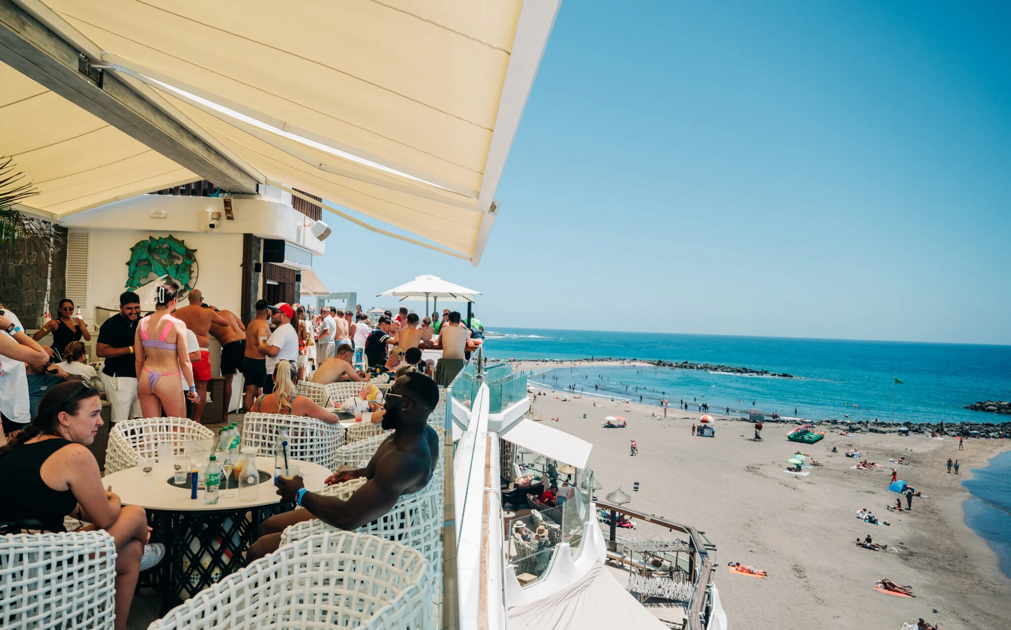Rooftop bar party in Tenerife overlooking the beach, packed crowd, day drinks flowing and holiday vibes turned up