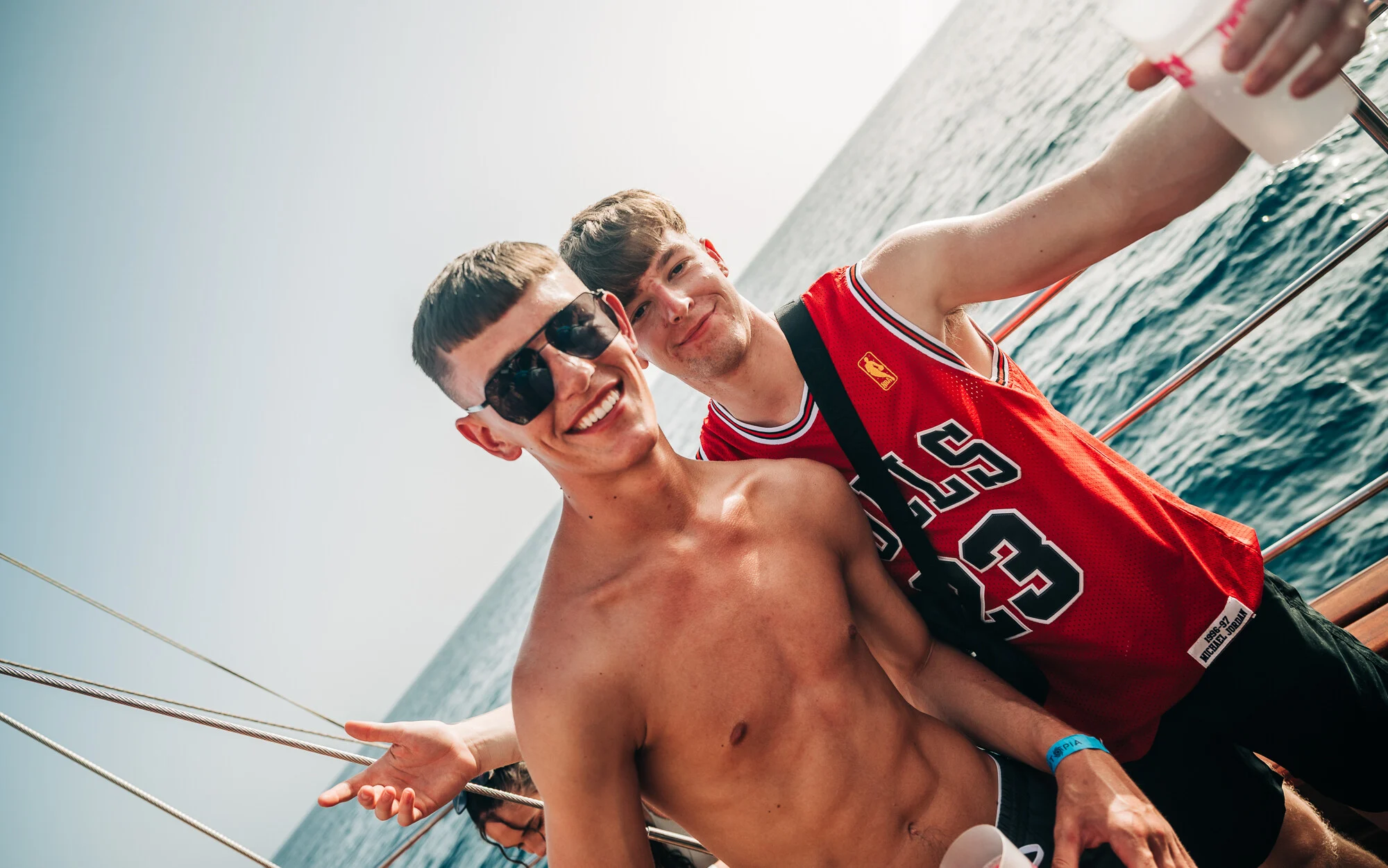 Two lads partying on a Tenerife boat trip, drinks in hand, sunshine blazing and holiday energy high on the open sea