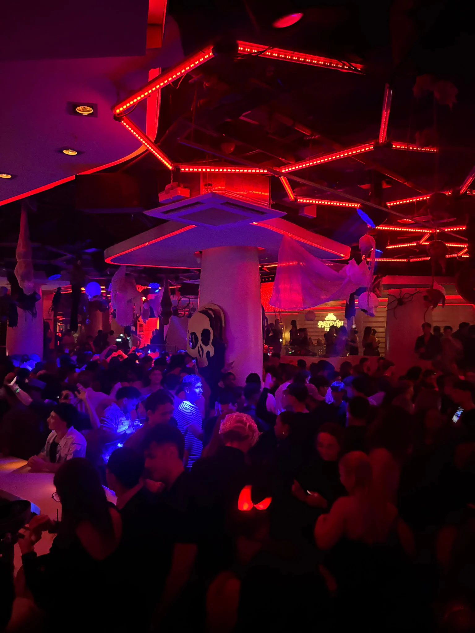Crowd packed into a Barcelona club under red neon lights, with people dancing and moving through the room as the night kicks off.