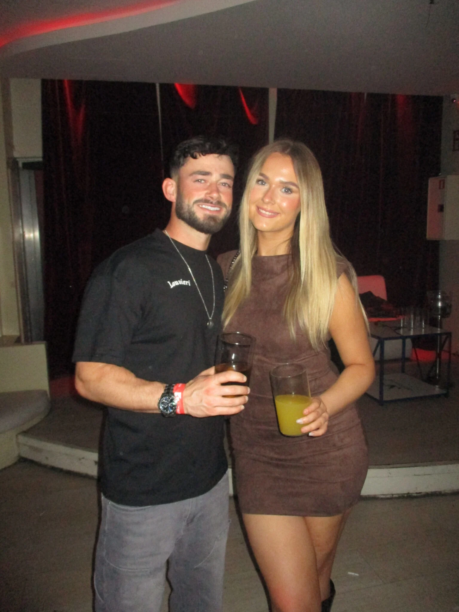 Lad and girl posing with drinks in a Barcelona club, smiling as they get set for another big night on the holiday schedule.