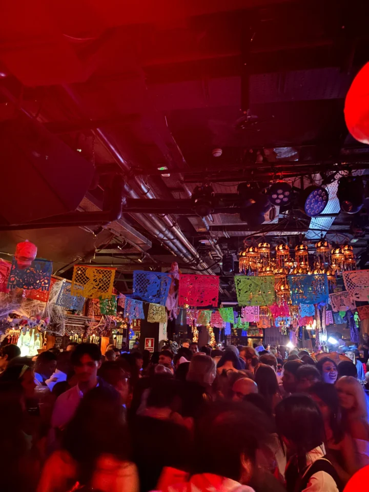 Crowd filling a Barcelona club decorated with bright papel picado, buzzing under red and neon lights all night.