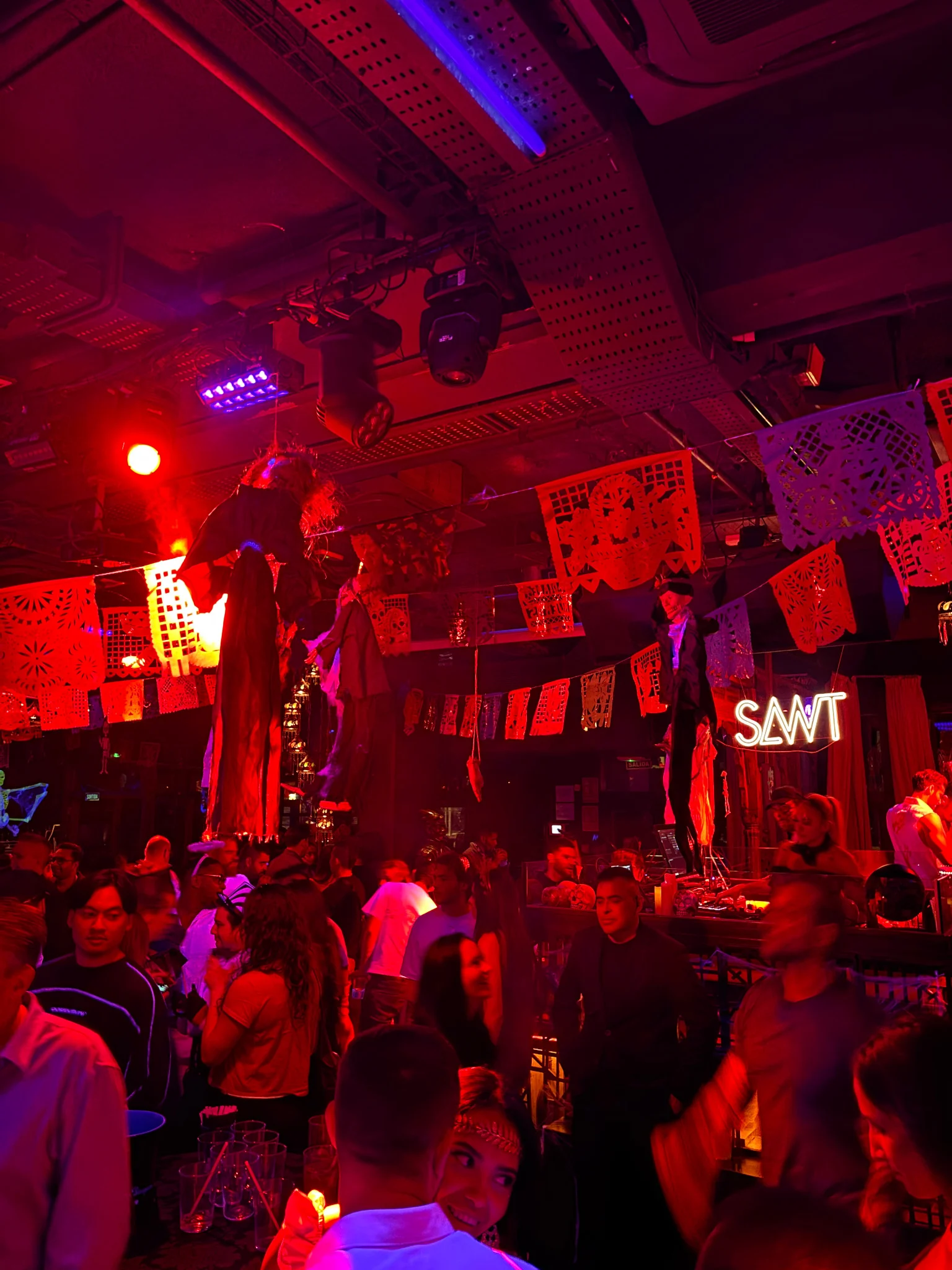 Crowd of lads and girls in a decorated Barcelona club, moving through red and neon lights as the DJ keeps the night buzzing.